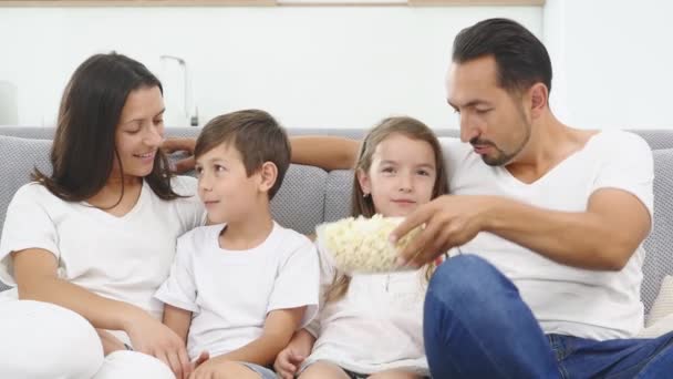 Happy family with two children relaxing at home, kids brother and sister watching a movie and having popcorn with parents - Filmati, video
