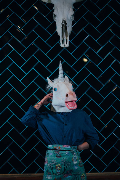 An unidentifiable people wears a White Rubber unicorn Head Mask in a Photo Booth with black  background. - Фото, изображение