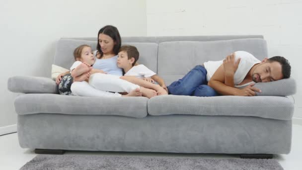 Los padres y sus hijos están viendo la televisión. Se sientan en un sofá en su acogedora sala de estar. Es de noche. mamá con niños habla cuando papá duerme. Vista inferior
 - Metraje, vídeo