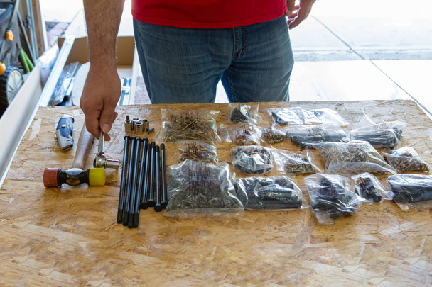 Homem verificando peças e suprimentos para um projeto DIY colocado ordenadamente em uma mesa na embalagem varejo original
 - Foto, Imagem