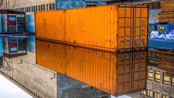Vista lateral de perto do contêiner de transporte laranja refletindo na poça. Armazém principal em Rijeka, Croácia
. - Foto, Imagem