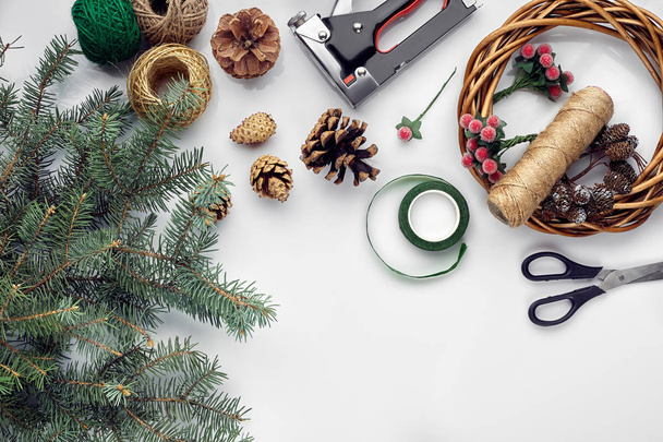 Preparing for Christmas or New Year holiday. Flat-lay of fur tree branches, wreaths, rope, scissors, craft paper over white table background, top view. - Photo, Image