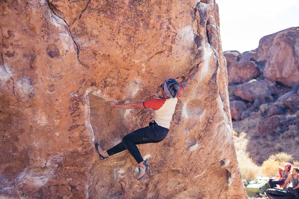Piccola donna asiatica arrampicata su roccia all'aperto pende da strapiombo di pietra con la gente a guardare
 - Foto, immagini