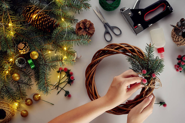 As mãos femininas decoram a grinalda de Natal com ramos de abeto com uma baga vermelha e cones florestais. Fundo branco. Conceito de Ano Novo
. - Foto, Imagem
