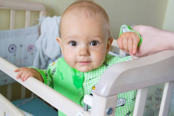 Ein einjähriges Baby sitzt da und schaut aufmerksam irgendwohin. kleiner fröhlicher Junge im hellgrünen Anzug mit Schafen. - Foto, Bild