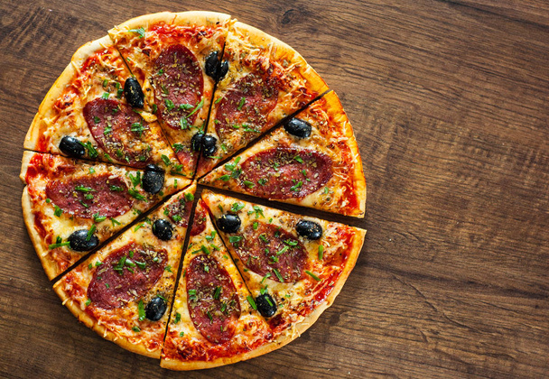 plasterki pizzy z ser Mozzarella, salami, papryka, pepperoni, oliwki, przyprawy i świeżą bazylią. Włoskiej pizzy na podłoże drewniane - Zdjęcie, obraz