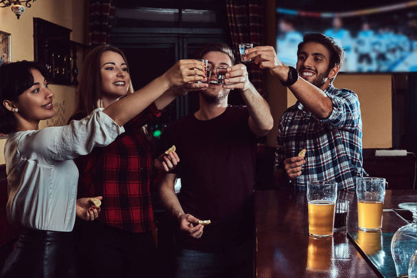 Boldog többnemzetiségű baráti pohárköszöntőt vodka állva a bárban vagy kocsmában. - Fotó, kép