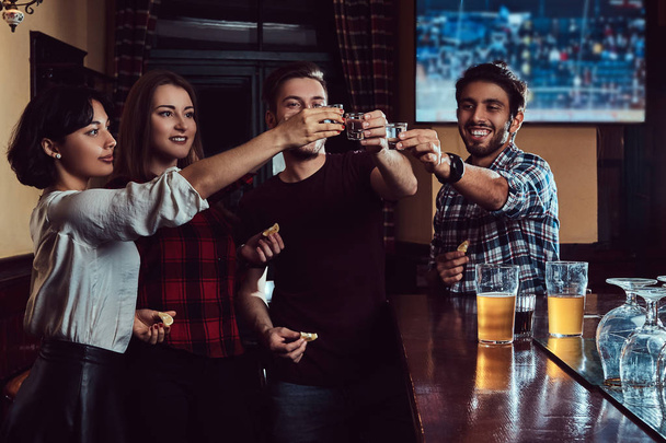 Groupe d'amis multiraciaux heureux faisant un toast avec de la vodka tout en se tenant au bar ou au pub
. - Photo, image