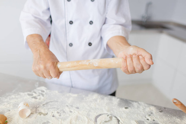 Close up of male baker hands kneading dough and making bread with a rolling pin in the kitchen - Fotografie, Obrázek