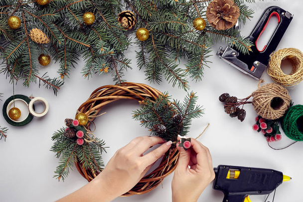 Las manos femeninas decoran la corona de Navidad con ramas de abeto con una baya roja y conos del bosque. Fondo blanco. Concepto de Año Nuevo
. - Foto, imagen