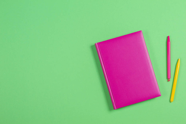 Pink hardcover book and colorful pens on green background - Foto, afbeelding