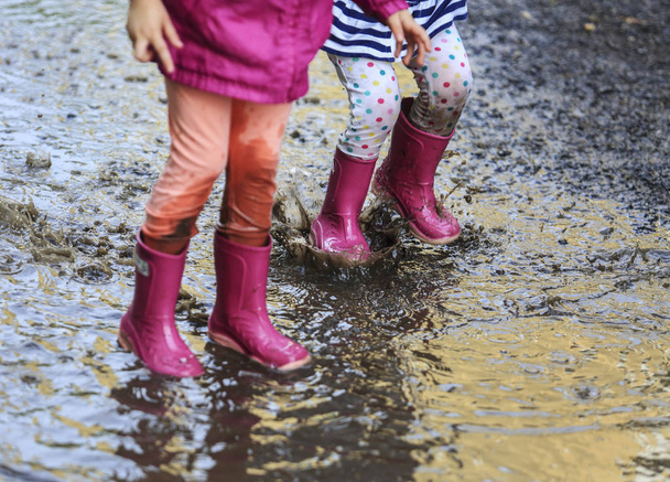 Παιχνιδιάρικο παιδί υπαίθρια άλμα σε λακκούβα σε μπότα μετά τη βροχή - Φωτογραφία, εικόνα