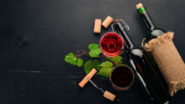 Red wine in a bottle with a glass and grapes. On a black wooden background. Free space for text. Top view. - Foto, afbeelding