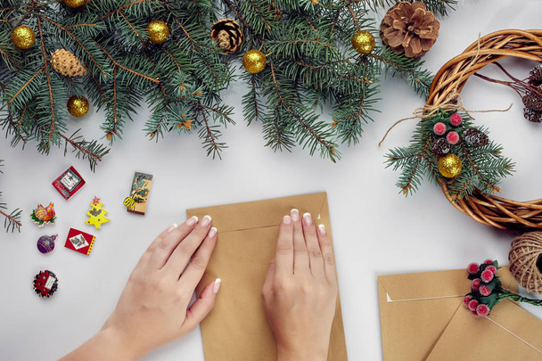 Frauenhände halten frohe Weihnachtskarte und Umschlag in der Hand. Weihnachtsdekoration Hintergrund. flache Lage, Draufsicht. - Foto, Bild