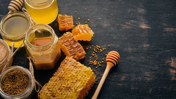Un ensemble de miel et de produits apicoles. Miel en nid d'abeille. Sur un fond en bois noir. Espace libre pour le texte. Vue du dessus
. - Photo, image