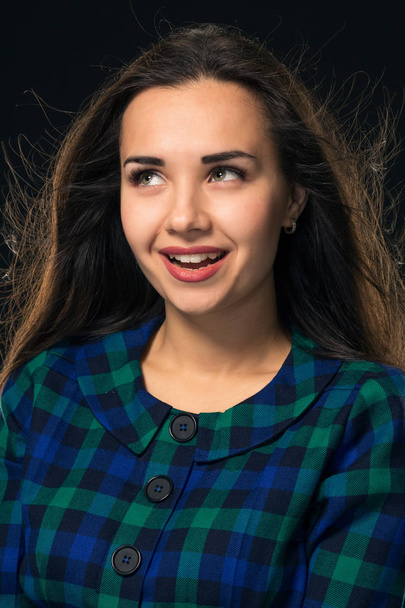 Portrait of cheerful attractive modern woman with long hair, expressing positive emotions while standing over black background. - Фото, зображення