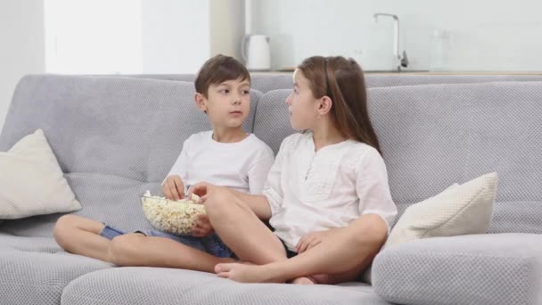 Cute children watching TV on sofa at home - Materiał filmowy, wideo