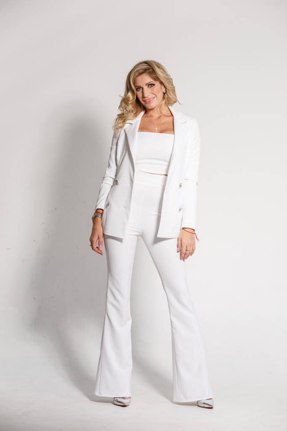 Fashion portrait of beautiful sexy blonde in white pants and white jacket on white studio background - Photo, Image