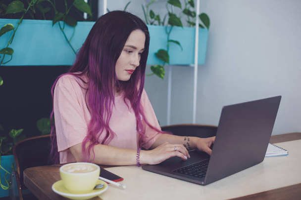 Jovem mulher com cabelo rosa com computador portátil sentado no café
, - Foto, Imagem