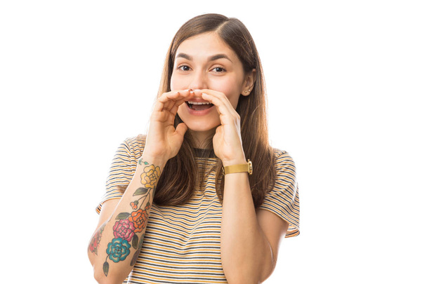 Mujer joven compartiendo secretos mientras cubre la boca con ambas manos contra fondo blanco
 - Foto, Imagen
