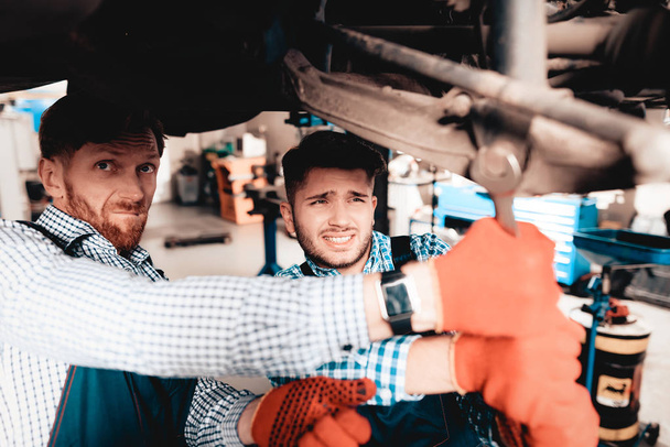 Young Mechanic Repairs Automotive Hub In Garage. Professional Uniform. Service Station Concept. Confident Engineer Stare. Detail Repairing. Under The Vehicle. Automobile Diagnostic. Join Forces. - Φωτογραφία, εικόνα