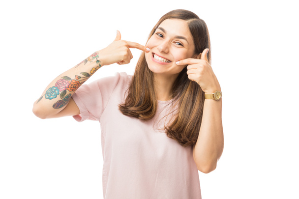 Zeker jonge vrouw toont haar perfect rechte witte tanden tegen witte achtergrond - Foto, afbeelding