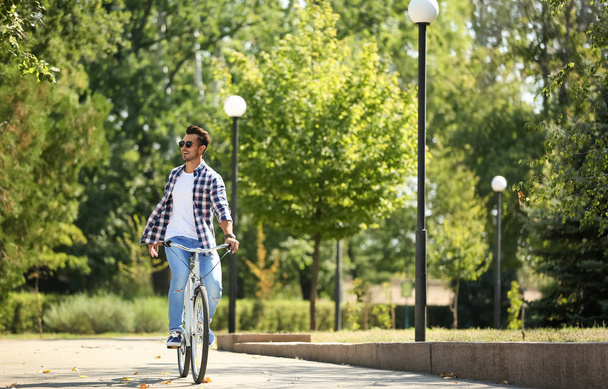 Handsome young hipster man riding bicycle in park - Photo, image