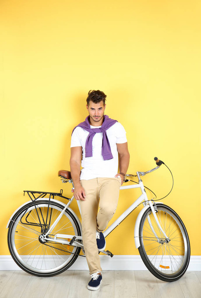Handsome young hipster man with bicycle near yellow wall - 写真・画像