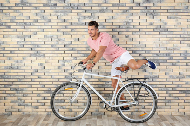 Handsome young hipster man riding bicycle near brick wall - Foto, afbeelding