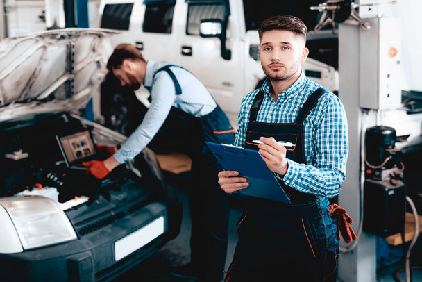 Young Mechanic Posing In Garage With Tablet Desk. Service Station Concept. Working Together In The Garage. Car Reparing With Wrench. Notes Making. Team Work. Automobile Diagnostic. - Φωτογραφία, εικόνα