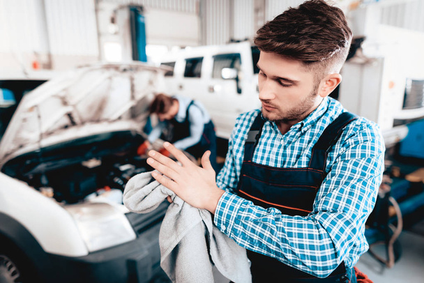 Young Auto Mechanic Wipes Hands With Towel In Garage. Service Station Concept. Working Together. Car Reparing With Wrench. Engineering Specialists. Team Work. Automobile Diagnostic. Dirty Hands. - Foto, Bild