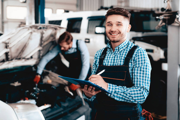 Young Mechanic Posing In Garage With Tablet Desk. Service Station Concept. Working Together In The Garage. Car Reparing With Wrench. Notes Making. Team Work. Automobile Diagnostic. - Photo, Image