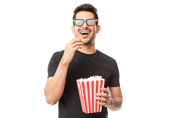 Улыбающийся молодой человек смотрит 3D фильм, поедая попкорн на белом фоне
 - Фото, изображение