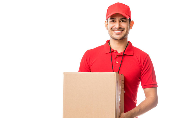 junger Arbeiter lächelt, während er Paket über weißem Hintergrund trägt - Foto, Bild