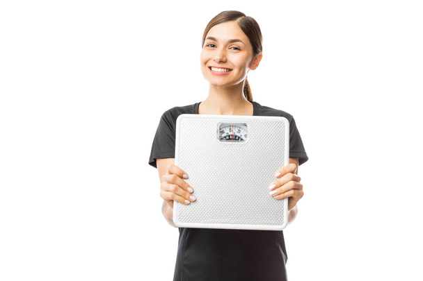 Beautiful healthy woman smiling while showing weight scale over white background - Valokuva, kuva