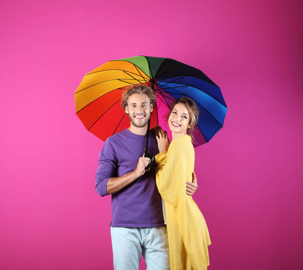 Couple with rainbow umbrella on color background - Foto, afbeelding