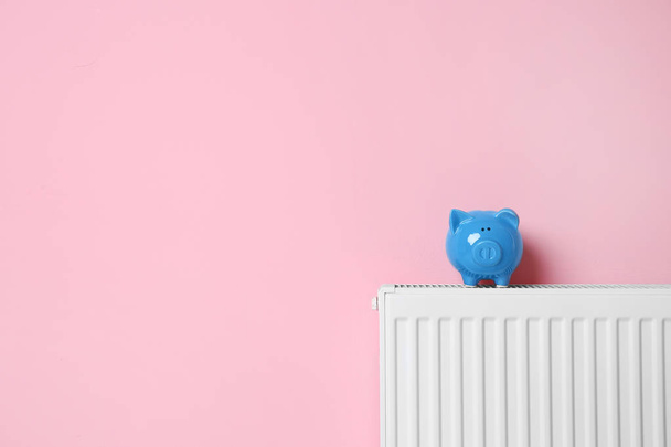 Heating radiator with piggy bank near color wall. Space for text - Foto, Imagen