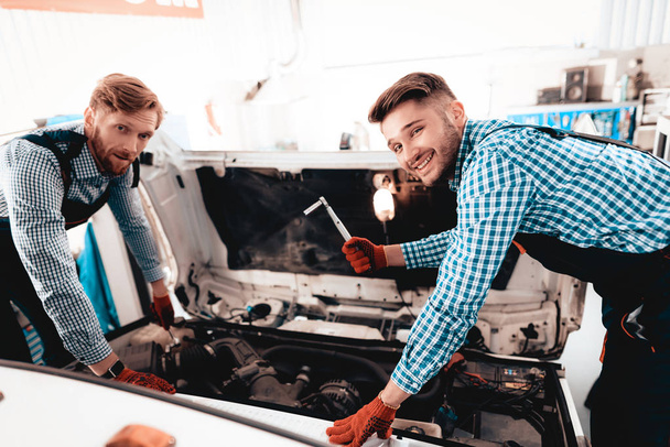 Two Auto Mechanics Are Looking Under The Hood. Professional Uniform. Confident Engineering Specialist Team Workers. Service Station Concept. Working Together In Garage. Wrench Using. - Φωτογραφία, εικόνα