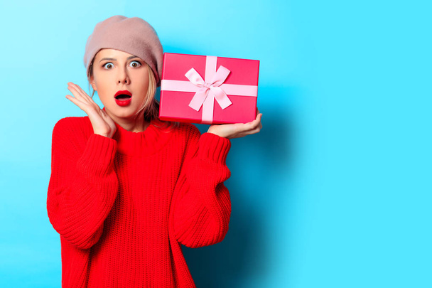 Portrait of a young girl in red sweater with gift box on blue background - Photo, Image