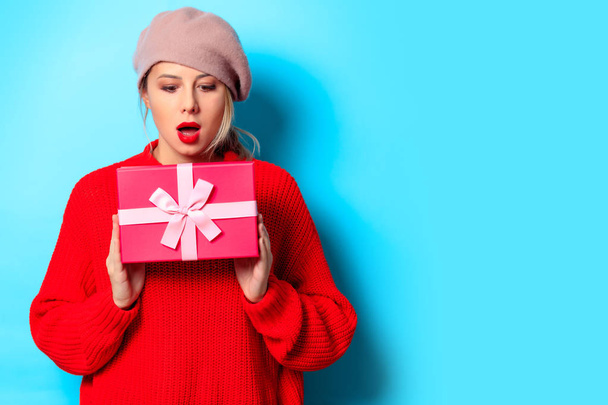 Portrait of a young girl in red sweater with gift box on blue background - Fotó, kép