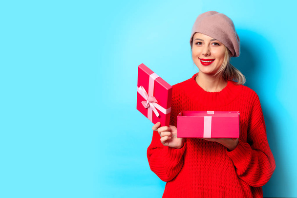 Porträt eines jungen Mädchens in rotem Pullover mit Geschenkbox auf blauem Hintergrund - Foto, Bild