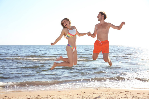 Happy young couple in beachwear jumping on seashore - Φωτογραφία, εικόνα