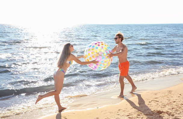 Happy young couple in beachwear playing with inflatable ball on seashore - Photo, image