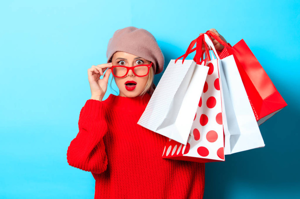 Portrait of a young girl in red sweater with shopping bags on blue background - Fotoğraf, Görsel