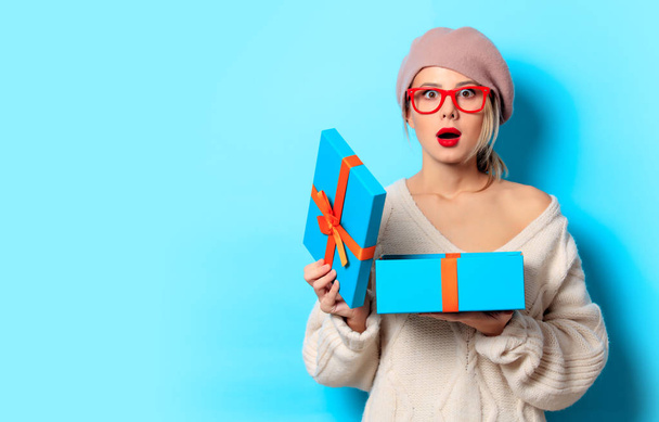 Portrait of a young girl in white sweater with gift box on blue background - Fotó, kép