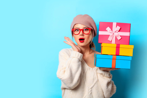 Portrait of a young girl in white sweater with gift colored boxes on blue background - Photo, Image
