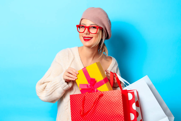 Portrait of a young girl in white sweater with gift box and shopping bags on blue background - Foto, Imagen