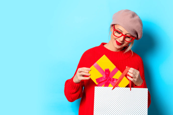 Ajándék doboz és bevásárló táska kék háttéren piros pulóver egy fiatal lány portréja - Fotó, kép