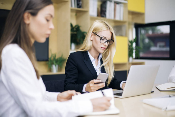 Portrait of attractive blond businesswomen working in modern office and uses mobile phone - Foto, imagen