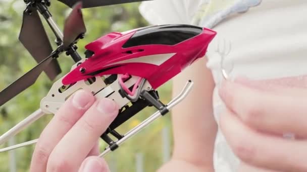 Males hand holds red nano toy helicopter and puts wedding ring on its skids - Footage, Video